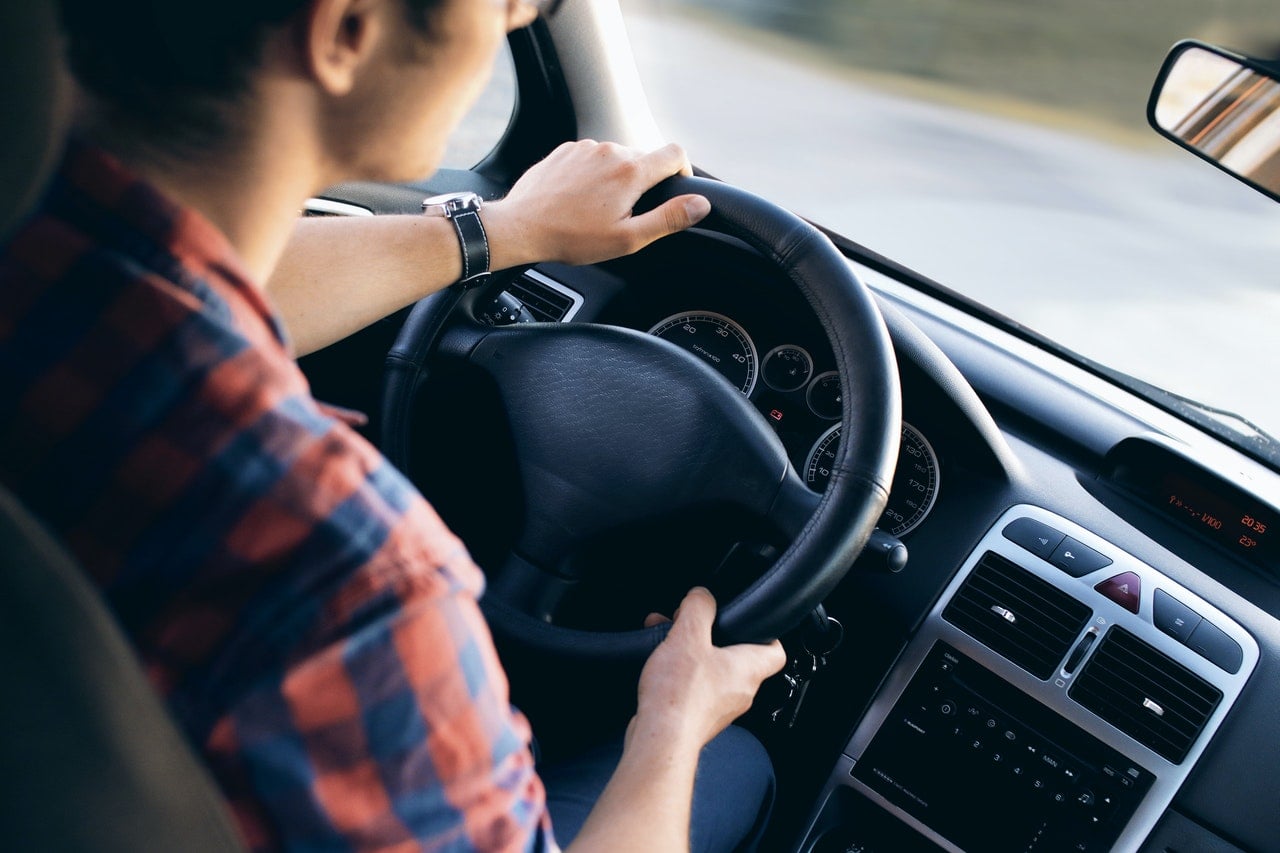 A driver is turning the steering wheel while driving a used car.